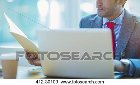 Focused businessman reviewing paperwork at laptop in office View Large Photo Image Stock Photo - Focused businessman reviewing paperwork at laptop in office. Fotosearch
