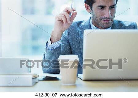 Focused businessman working at laptop in office View Large Photo Image Stock Photo - Focused businessman working at laptop in office. Fotosearch