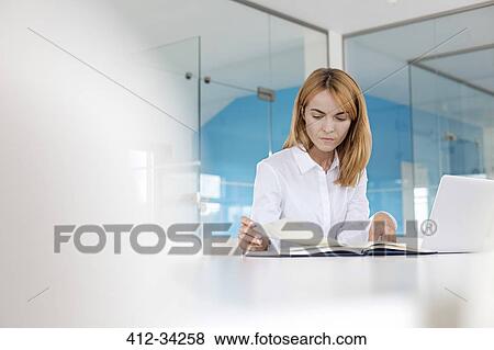 Focused businesswoman reviewing paperwork at laptop in conference room View Large Photo Image Stock Photo - Focused businesswoman reviewing paperwork at laptop in conference room. Fotosearch