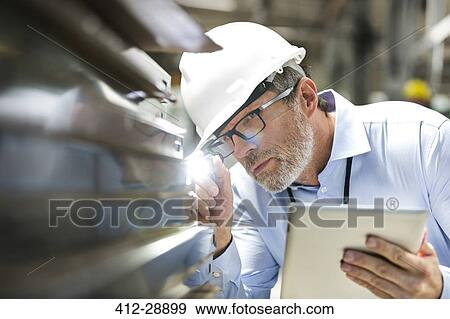 Focused engineer with digital tablet and flashlight examining part in factory View Large Photo Image Stock Photo - Focused engineer with digital tablet and flashlight examining part in factory. Fotosearch