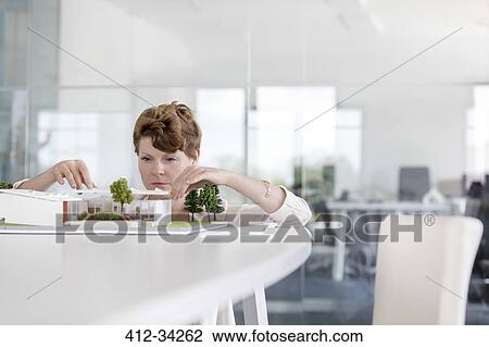 Stock Image - Focused female architect arranging model in conference room. Fotosearch