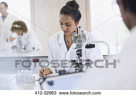 Stock Image - Focused female college student conducting scientific experiment at microscope in science laboratory classroom. Fotosearch