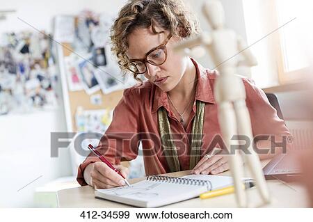 Stock Photo - Focused female design professional sketching in notebook in office. Fotosearch