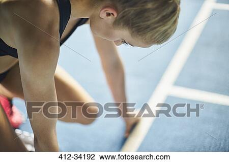 Stock Image - Focused female runner ready at starting block on sports track. Fotosearch