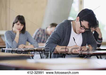 Stock Image - Focused male college student taking test at desk in classroom. Fotosearch