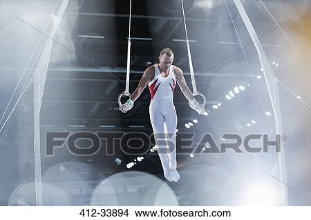 Focused male gymnast performing on gymnastics rings in arena View Large Photo Image Picture - Focused male gymnast performing on gymnastics rings in arena. Fotosearch