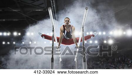 Picture - Focused male gymnast performing splits on parallel bars in arena. Fotosearch