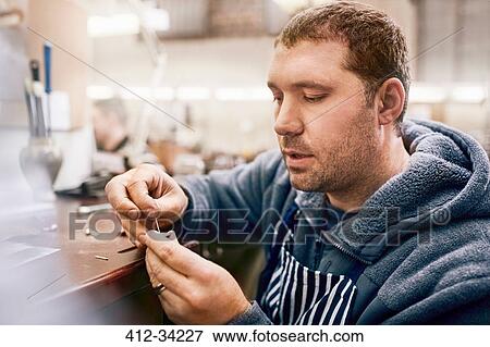 Stock Photo - Focused male jeweler making jewelry in workshop. Fotosearch