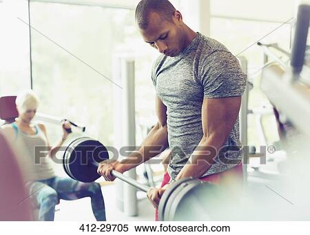 Stock Photography - Focused man doing barbell biceps curls at gym. Fotosearch