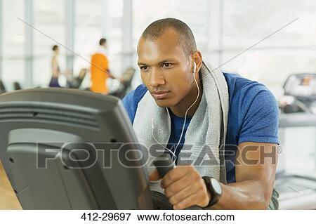 Stock Photo - Focused man riding exercise bike at gym. Fotosearch