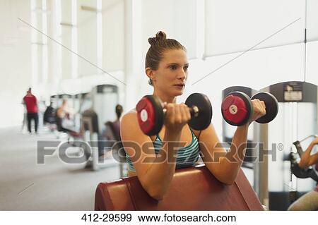 Focused woman doing dumbbell biceps curls at gym View Large Photo Image Stock Photo - Focused woman doing dumbbell biceps curls at gym. Fotosearch