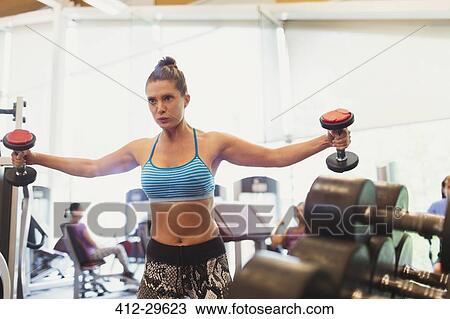 Stock Image - Focused woman doing dumbbell chest fly at gym. Fotosearch