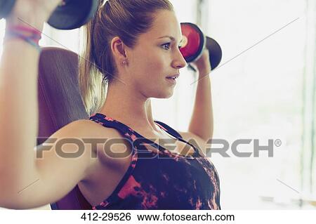 Stock Photograph - Focused woman doing dumbbell shoulder presses. Fotosearch