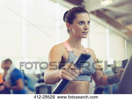 Stock Photo - Focused woman exercising on elliptical trainer in gym. Fotosearch