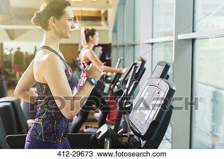 Stock Image - Focused woman running on treadmill at gym. Fotosearch