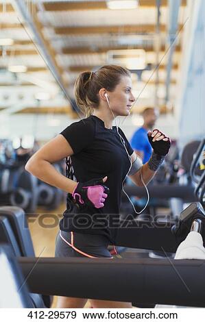 Stock Photo - Focused woman running on treadmill at gym. Fotosearch
