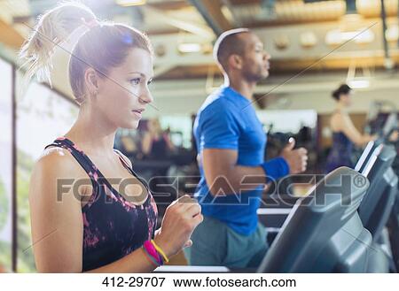 Stock Photo - Focused woman running on treadmill at gym. Fotosearch