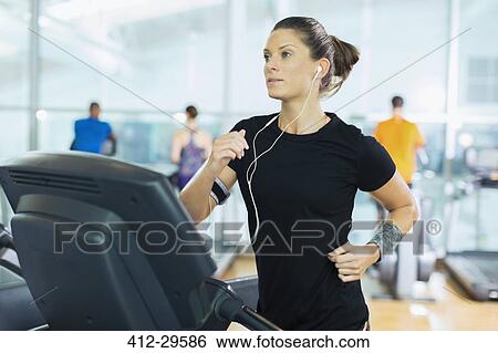Focused woman running on treadmill with headphones at gym View Large Photo Image Stock Photograph - Focused woman running on treadmill with headphones at gym. Fotosearch