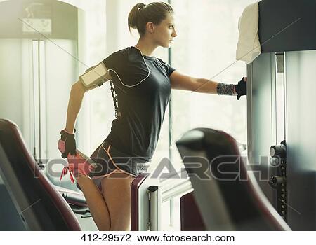 Stock Image - Focused woman stretching leg at exercise equipment in gym. Fotosearch