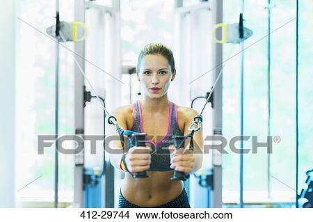 Picture - Focused woman using cable exercise equipment at gym. Fotosearch