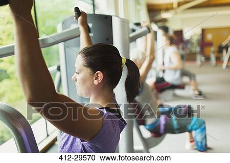 Focused woman using exercise equipment at gym View Large Photo Image Stock Image - Focused woman using exercise equipment at gym. Fotosearch