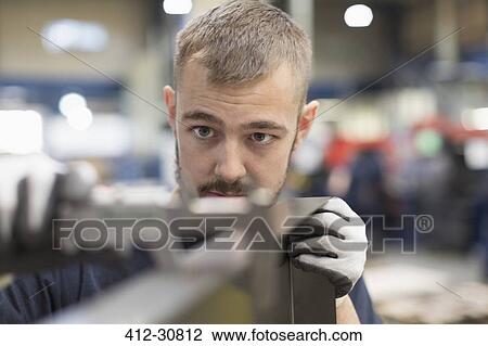 Stock Image - Focused worker examining part in steel factory. Fotosearch