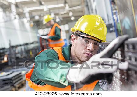 Focused worker examining steel part in factory View Large Photo Image Stock Photography - Focused worker examining steel part in factory. Fotosearch