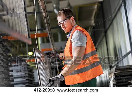 Stock Photo - Focused worker holding steel part in factory. Fotosearch