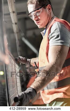 Focused worker holding steel part in factory View Large Photo Image Stock Photo - Focused worker holding steel part in factory. Fotosearch