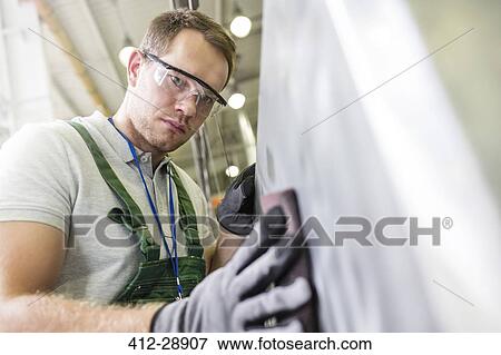 Focused worker sanding part in factory View Large Photo Image Stock Photo - Focused worker sanding part in factory. Fotosearch
