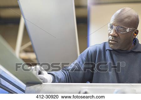 Stock Image - Focused worker sanding steel in steel factory. Fotosearch