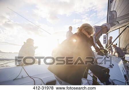 Friends adjusting sailing equipment on sunny sailboat View Large Photo Image Stock Photo - Friends adjusting sailing equipment on sunny sailboat. Fotosearch