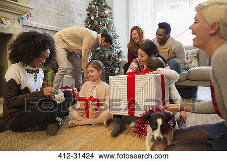 Picture - Friends and family opening Christmas gifts in living room. Fotosearch