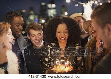 Stock Image - Friends celebrating young womans birthday with cake and candles. Fotosearch