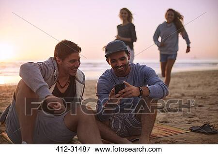 Friends hanging out texting with cell phone on sunset beach View Large Photo Image Stock Photo - Friends hanging out texting with cell phone on sunset beach. Fotosearch