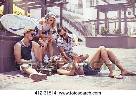 Picture - Friends hanging out using digital tablet on sunny sidewalk. Fotosearch