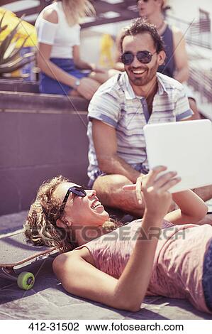 Friends hanging out using digital tablet on skateboard View Large Photo Image Stock Image - Friends hanging out using digital tablet on skateboard. Fotosearch
