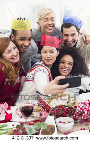 Friends in paper crowns taking selfie at Christmas dinner View Large Photo Image Stock Photo - Friends in paper crowns taking selfie at Christmas dinner. Fotosearch