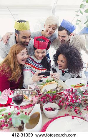 Friends in paper crowns taking selfie at Christmas dinner View Large Photo Image Stock Photo - Friends in paper crowns taking selfie at Christmas dinner. Fotosearch