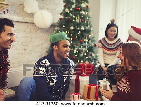 Friends opening Christmas gifts in living room View Large Photo Image Stock Image - Friends opening Christmas gifts in living room. Fotosearch