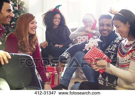 Stock Photo - Friends opening Christmas gifts in living room. Fotosearch