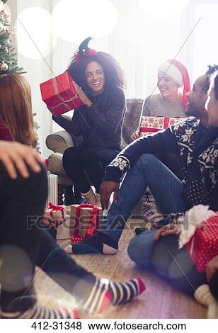 Stock Photo - Friends opening Christmas gifts in living room. Fotosearch