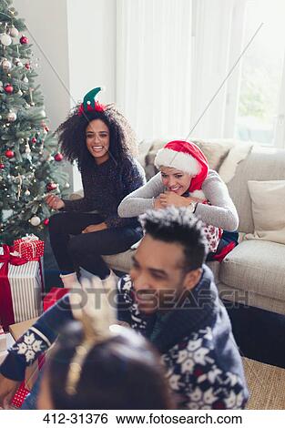 Friends opening Christmas gifts in living room View Large Photo Image Stock Photograph - Friends opening Christmas gifts in living room. Fotosearch