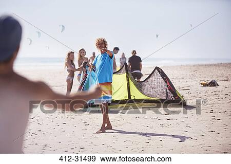 Stock Photo - Friends preparing kiteboarding kite on sunny beach. Fotosearch