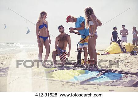 Stock Photo - Friends preparing kiteboarding kite on sunny beach. Fotosearch