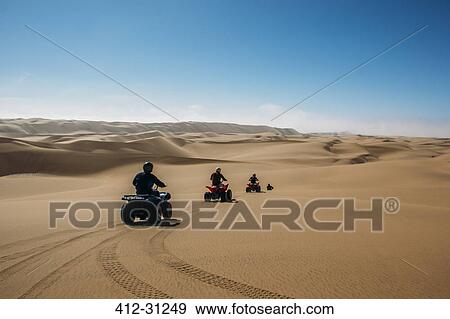 Stock Photo - Friends riding quadbikes in sunny desert, Swakopmund, Namibia. Fotosearch