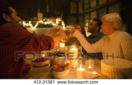 Stock Photo - Friends toasting champagne glasses at candlelight Christmas dinner party. Fotosearch