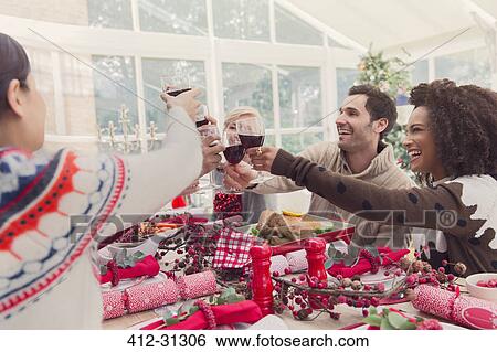 Stock Photograph - Friends toasting wine glasses at Christmas table. Fotosearch