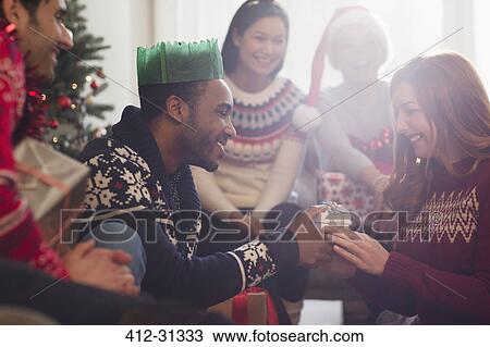 Stock Image - Friends watching boyfriend giving Christmas gift to girlfriend. Fotosearch
