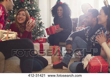 Friends watching playful woman shaking Christmas gift View Large Photo Image Stock Image - Friends watching playful woman shaking Christmas gift. Fotosearch